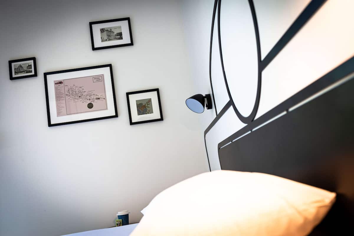 Un dormitorio con cama, lámpara de pared y cuadros enmarcados.