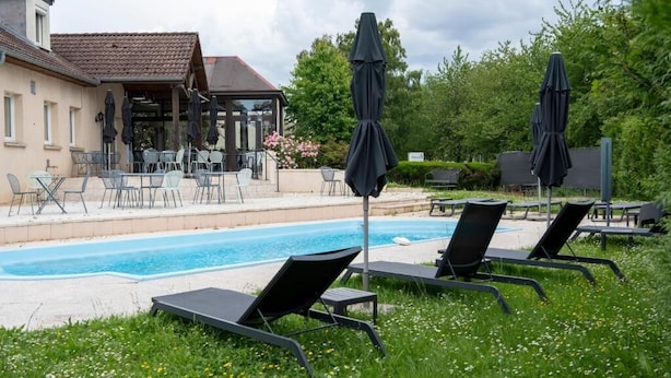 A pool area with lounge chairs and umbrellas, a covered seating area, and a building with a tiled roof. - Kyriad Nuits-Saint-Georges (Nuits-Saint-Georges)