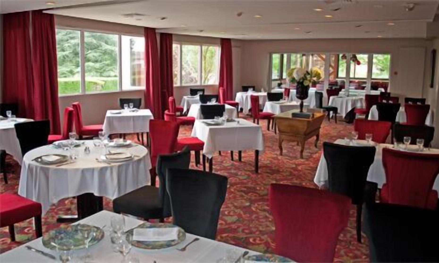 A dining area with round tables, red chairs, and large windows with red curtains.