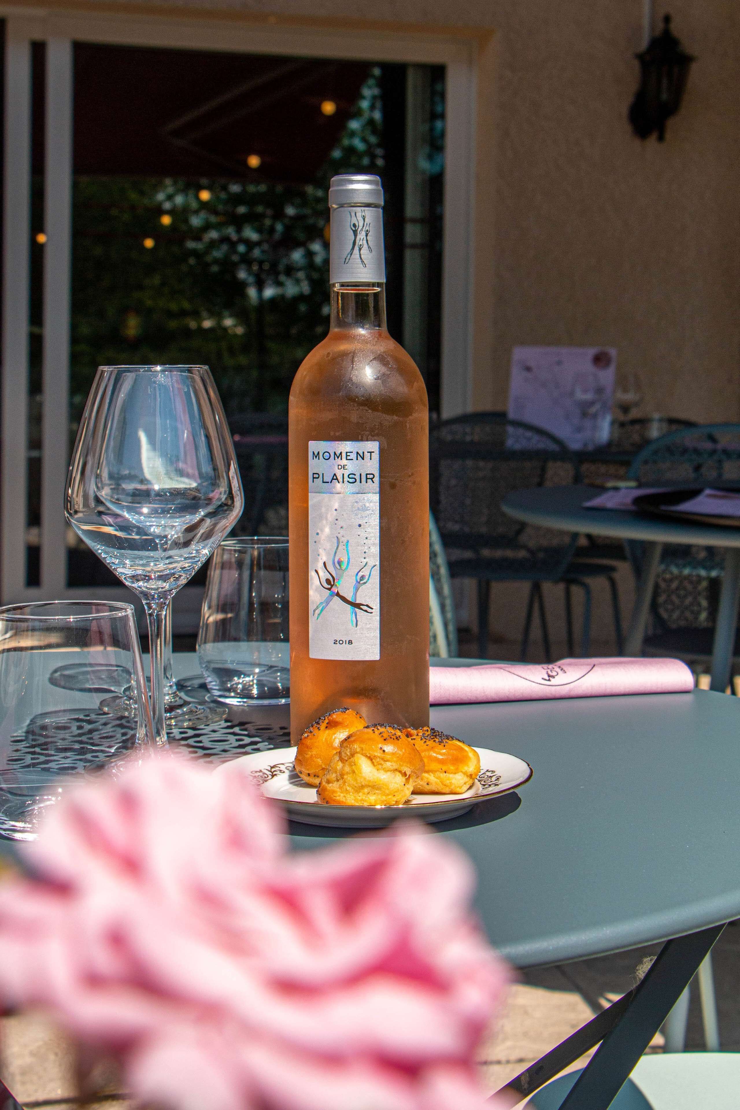 A bottle of Moment de Plaisir wine, a glass, and a plate with pastries on a table.