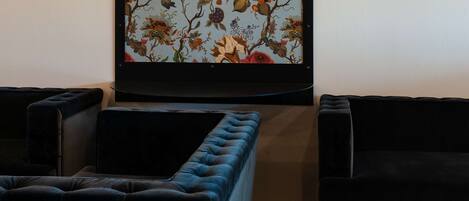 Una habitación con un ventanal de gran tamaño con estampado floral, una zona de estar con cojines y una revista sobre una mesita.