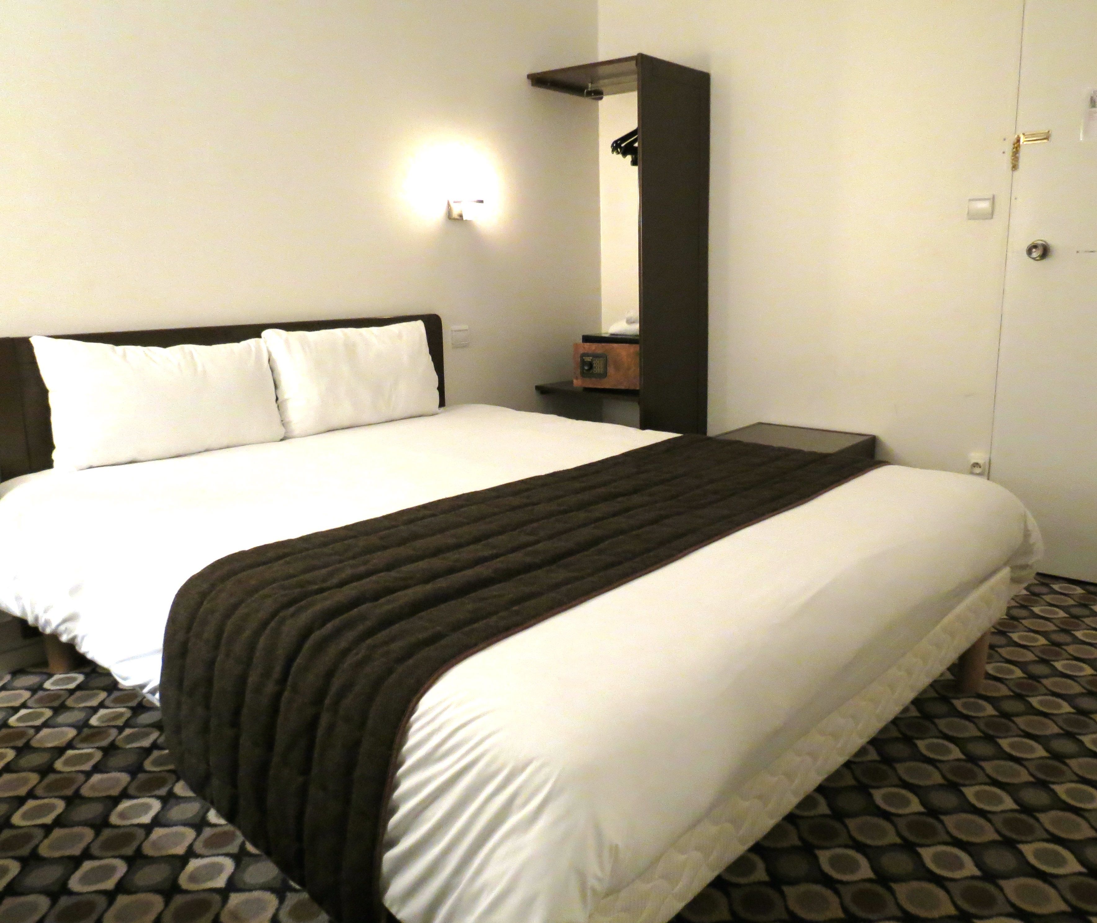 Una habitación de hotel con una cama grande, una mesita de noche con radio y un armario.