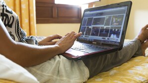 A person using a laptop on a bed with a yellow patterned bedspread. - Hostal Loreto (Denia)