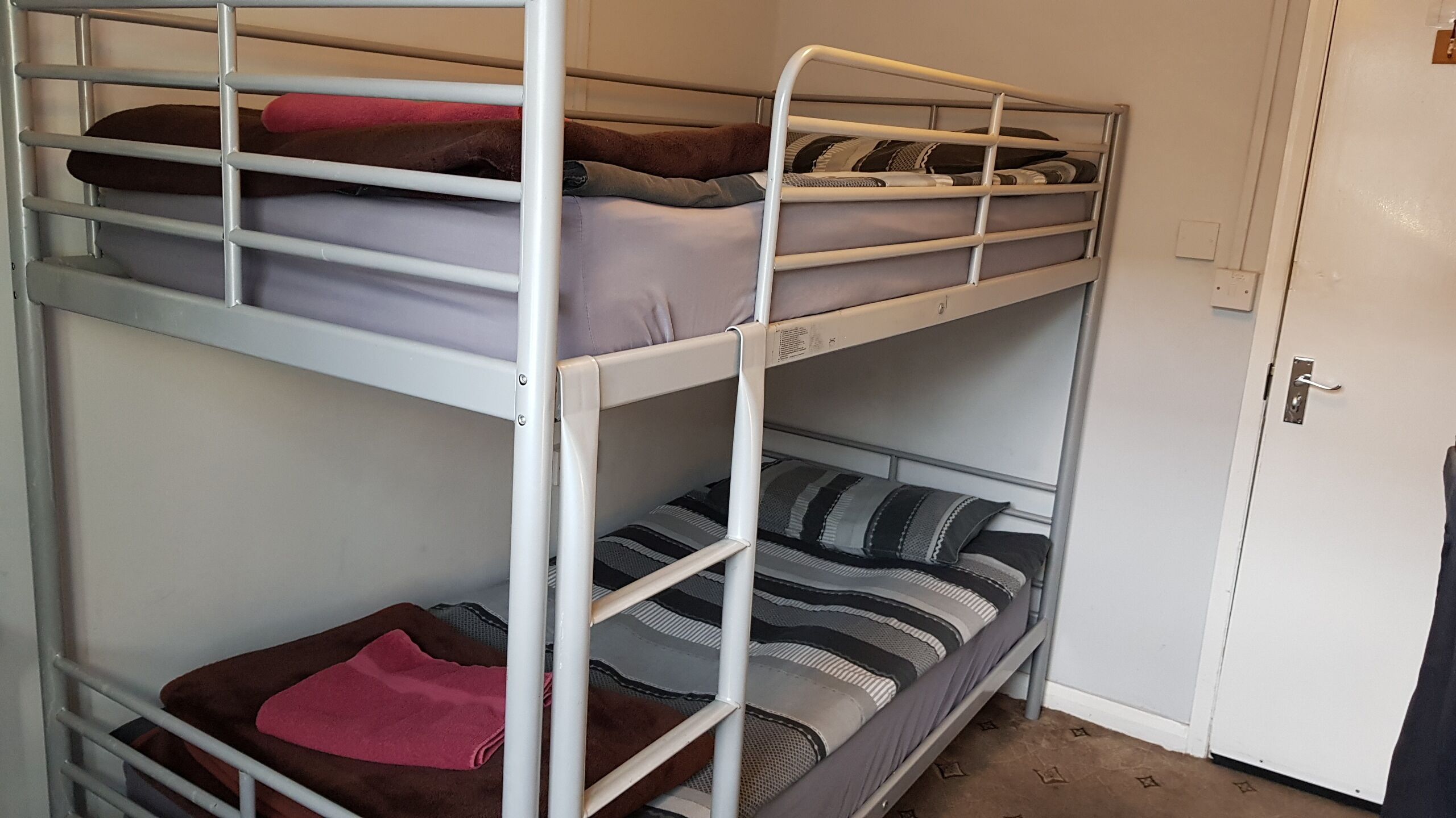 Ein Etagenbett mit drei Schlafstellen, jede mit einer andersfarbigen Decke.