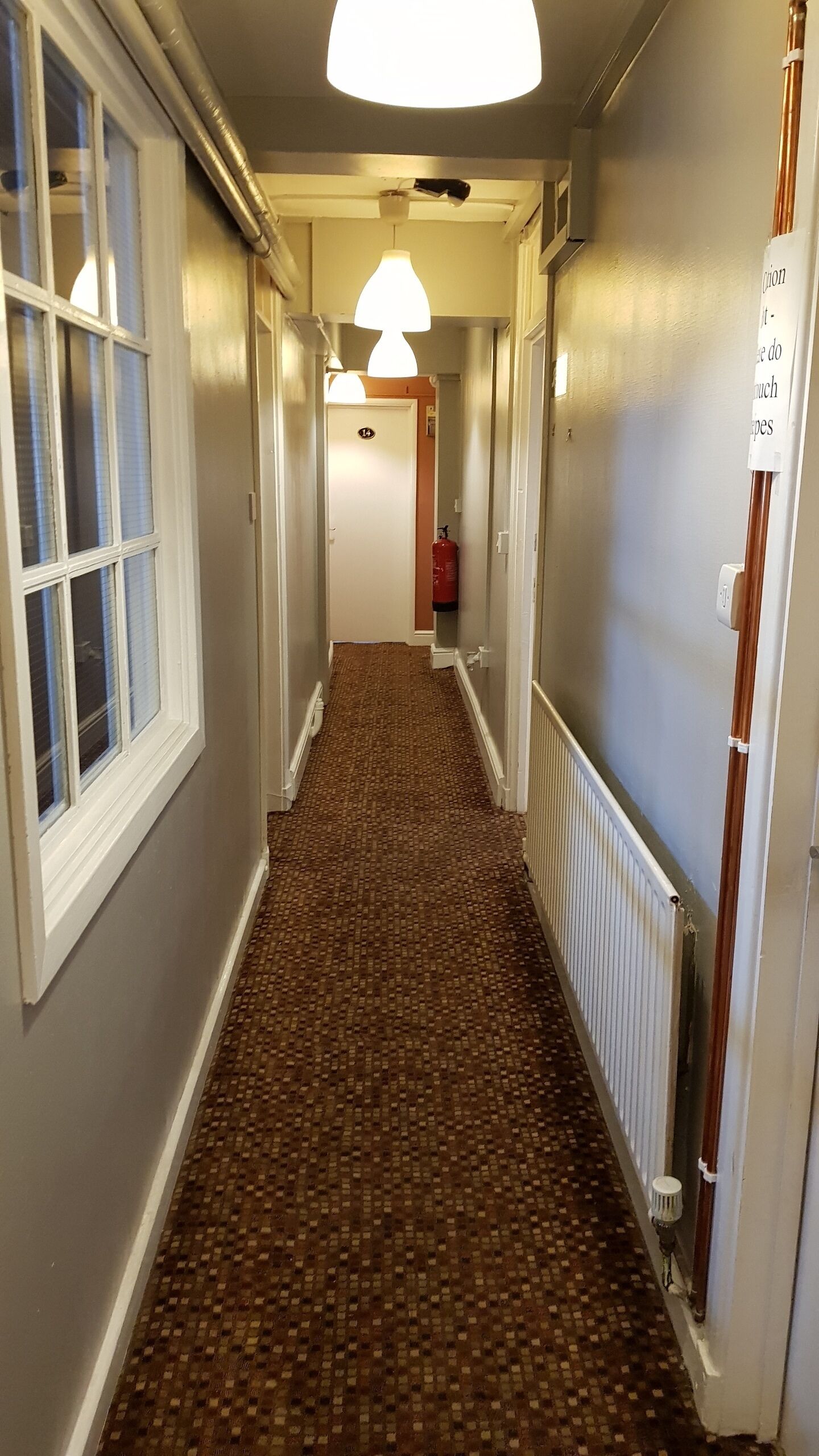 A hallway with patterned carpet, white walls, and a door marked with the number 14.
