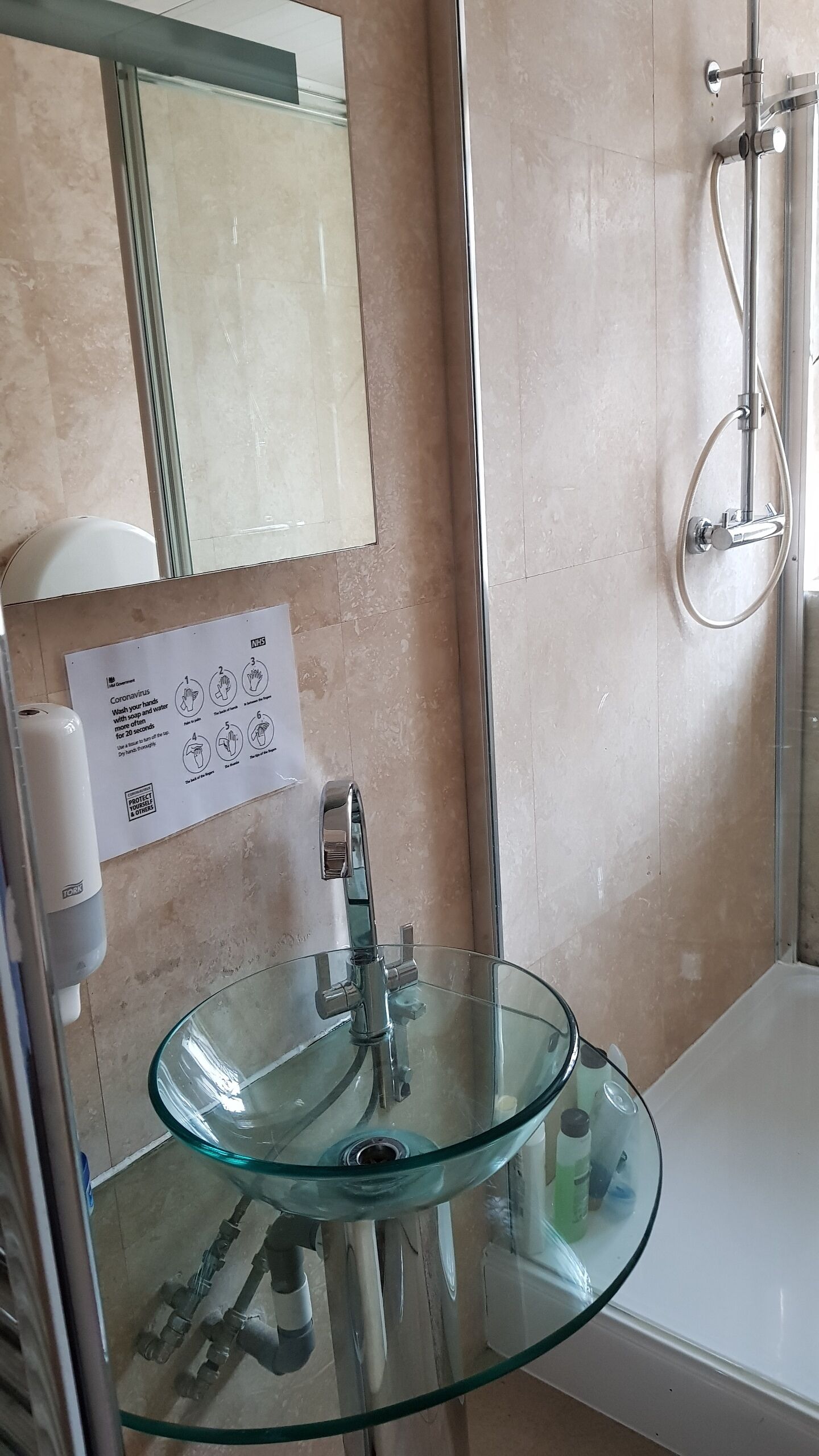 A bathroom with a glass sink, a mirror, a hand sanitizer dispenser, and a shower.
