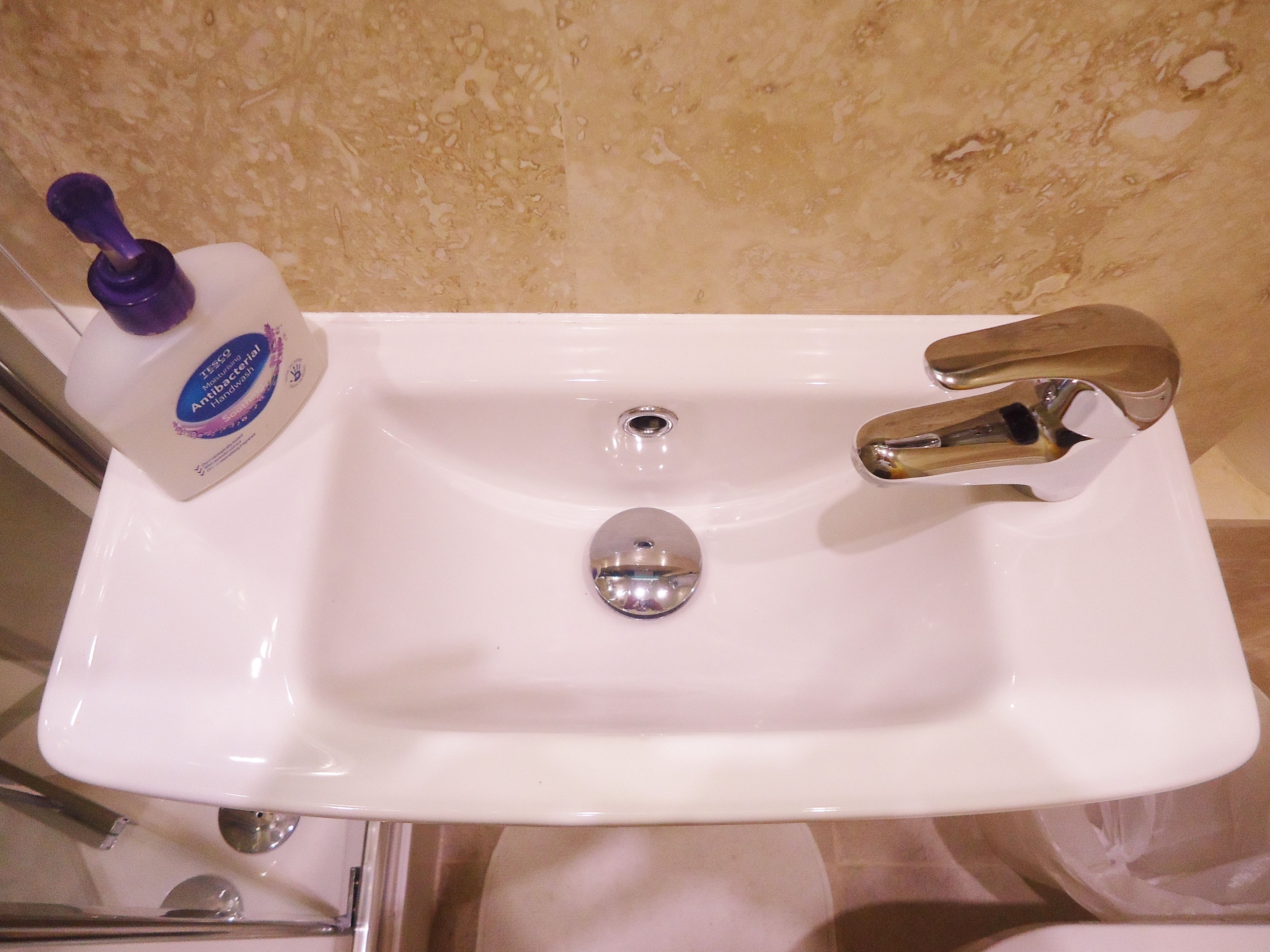 A white bathroom sink with a single faucet and a bottle of hand soap.
