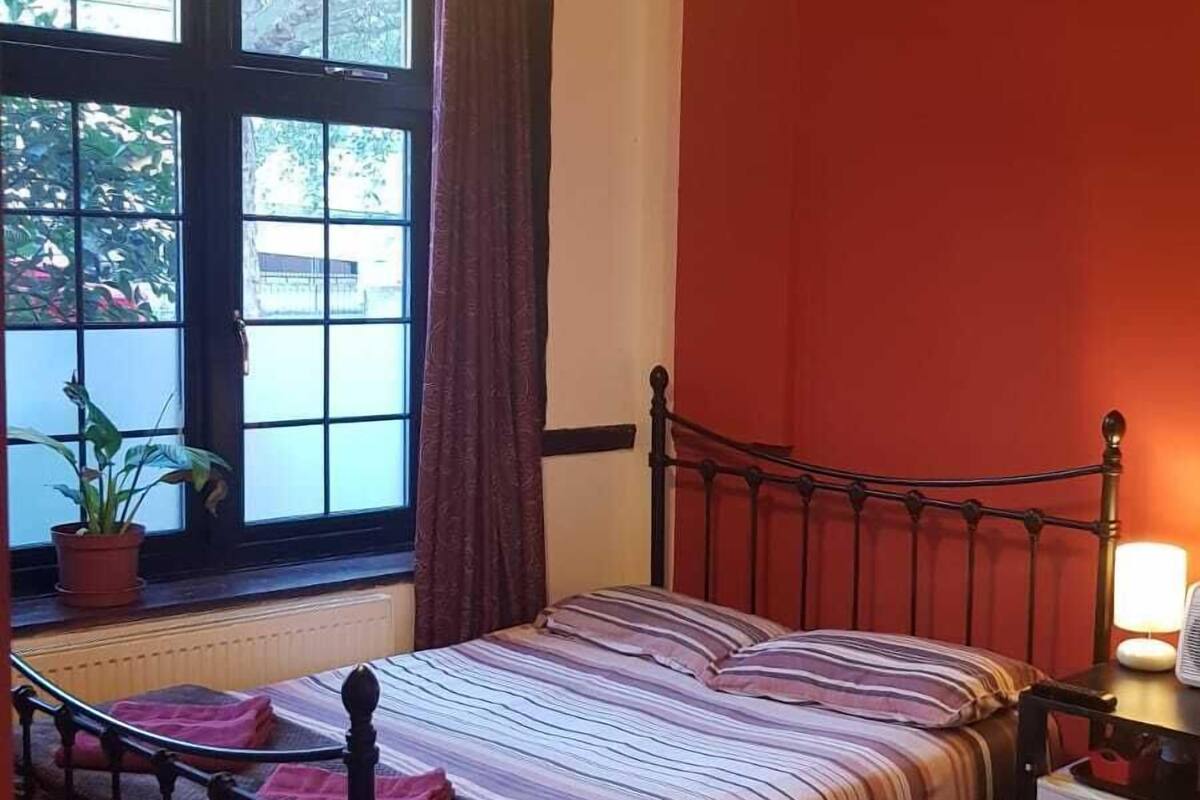 A bedroom with a bed, a chair, a window with curtains, and a lamp.