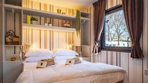 Une chambre à coucher bien rangée, avec un lit, des tables de chevet, une étagère ornée d’objets décoratifs et une fenêtre avec des rideaux.