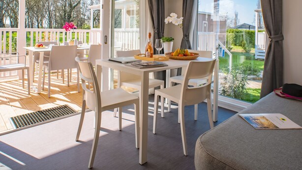 Une pièce lumineuse, avec une table à manger, des chaises, un téléviseur et une vue sur l’extérieur.