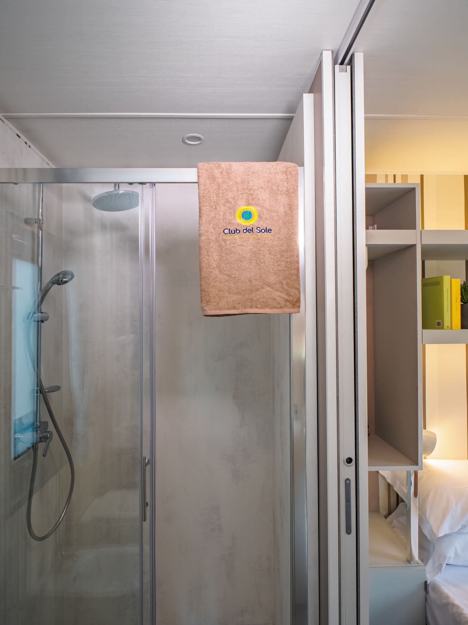 Ein Hotelzimmer mit Duschkabine aus Glas, einem Handtuch, das an der Tür hängt, und einem Bett mit weißer Bettwäsche.