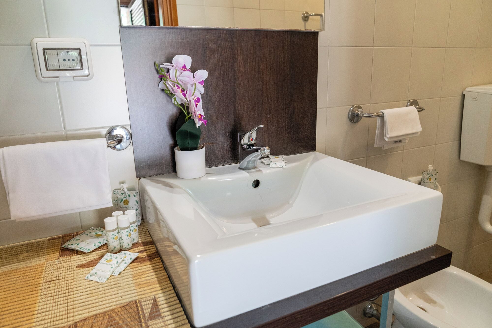 A bathroom with a white sink, a mirror, a towel rack, and a small potted orchid.