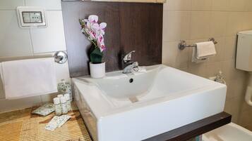 A bathroom with a white sink, a mirror, a towel rack, and a small potted orchid.