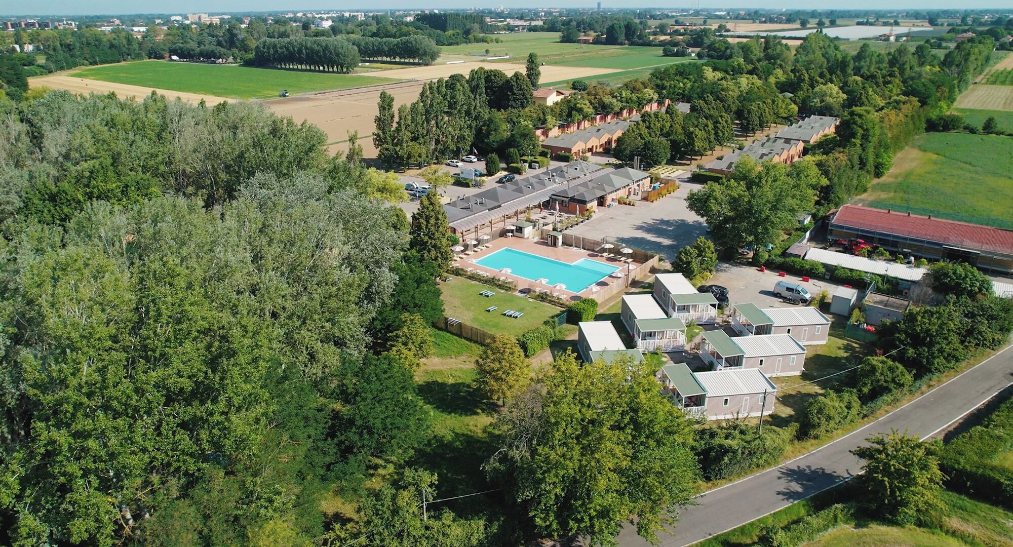 An aerial view of a residential area with a swimming pool, multiple houses, and surrounding greenery.