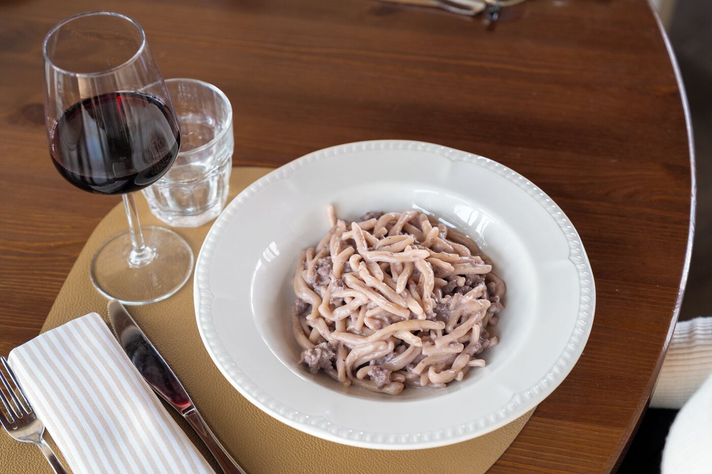 A plate of pasta with a glass of red wine and a napkin on a table.