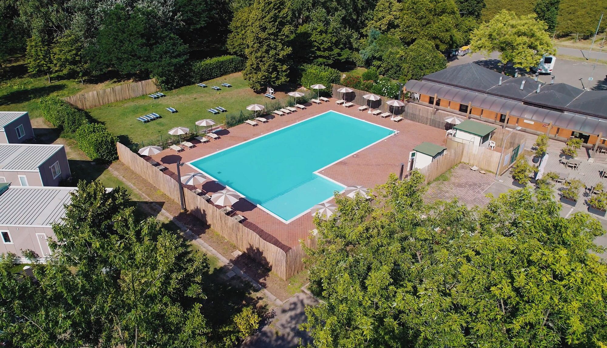 An aerial view of a swimming pool surrounded by a fence, with adjacent buildings and trees.