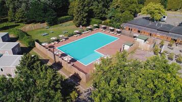 An aerial view of a swimming pool surrounded by a fence, with adjacent buildings and trees.