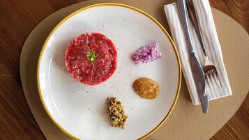 A plate with a red meat dish, a small pile of red onion, and a brown sauce, accompanied by a fork and knife on a beige napkin.