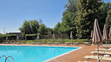 Una piscina al aire libre, sombrillas, sillones reclinables de piscina