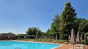Une piscine rectangulaire, bordée d’une terrasse carrelée, entourée de chaises longues et de parasols.