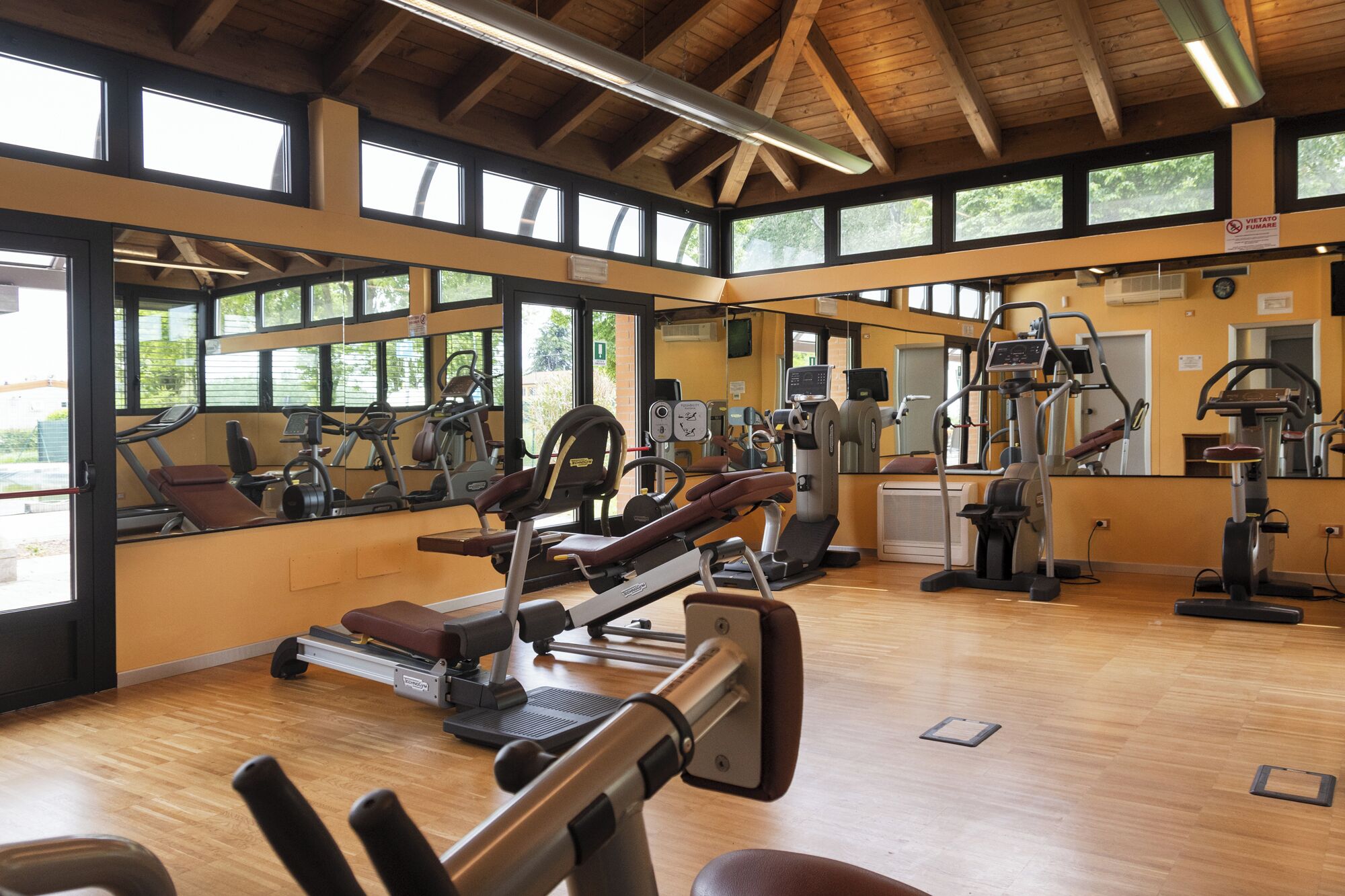 Ett gym med träningsutrustning, stora fönster och ett träpanelat tak.