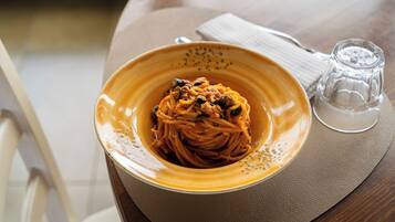 A bowl of spaghetti with a tomato-based sauce, a clear glass, and a napkin on a table.