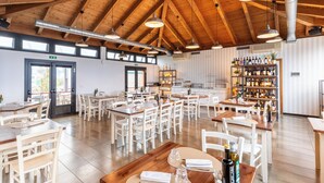 Un restaurant spacieux avec de hauts plafonds en bois, de nombreuses tables et un bar à vin bien fourni.