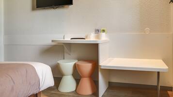 A hotel room with a bed, a small white table, two stools, and a mounted TV.