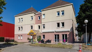 Un hotel con un letrero amarillo que indica un área de estacionamiento, un edificio rojo a la izquierda y un cielo azul despejado.