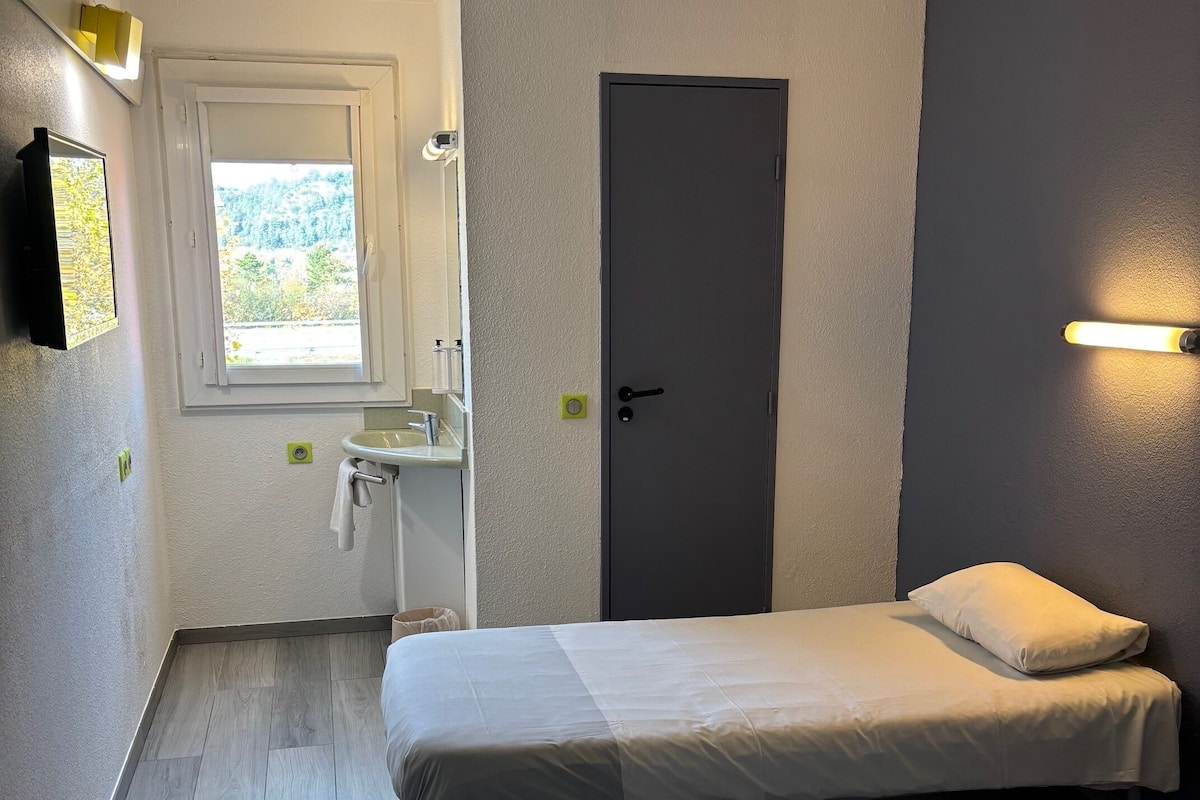 Une chambre avec deux lits, une fenêtre, un lavabo et une porte.