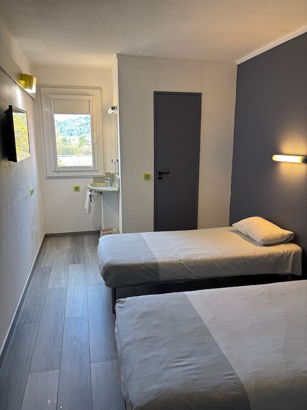 A bedroom with two beds, a window, a sink, and a door.