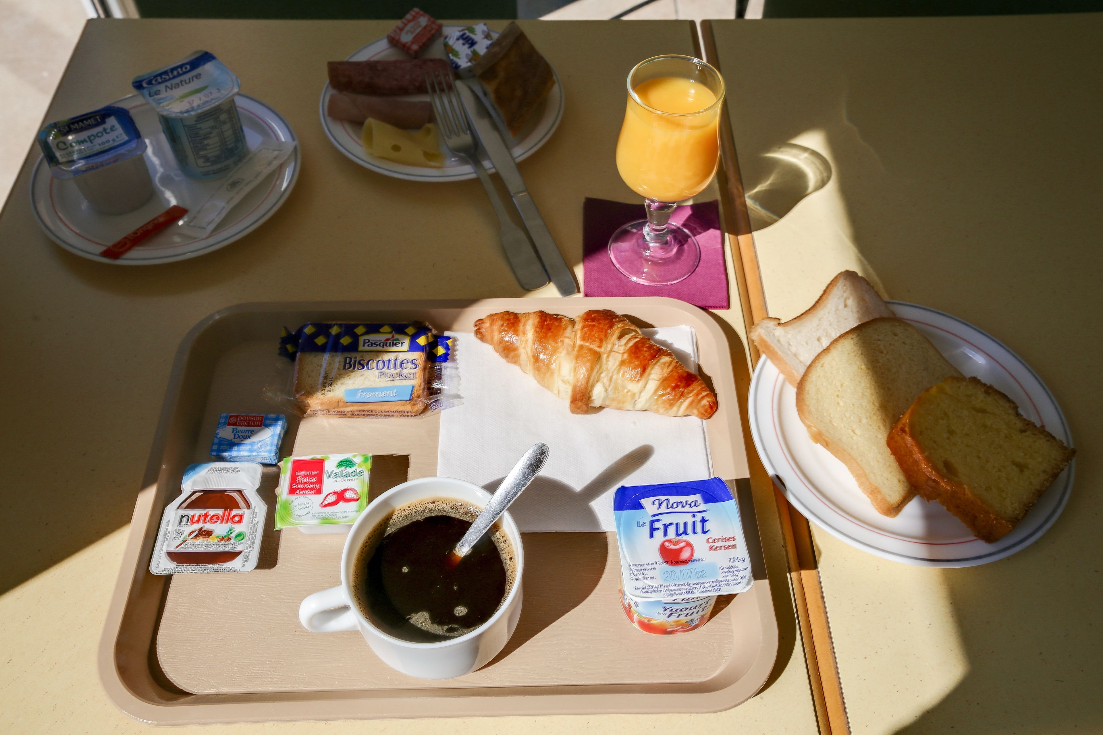Un plateau de petit-déjeuner avec des croissants, du pain, du jus de fruits, du café et diverses confitures.