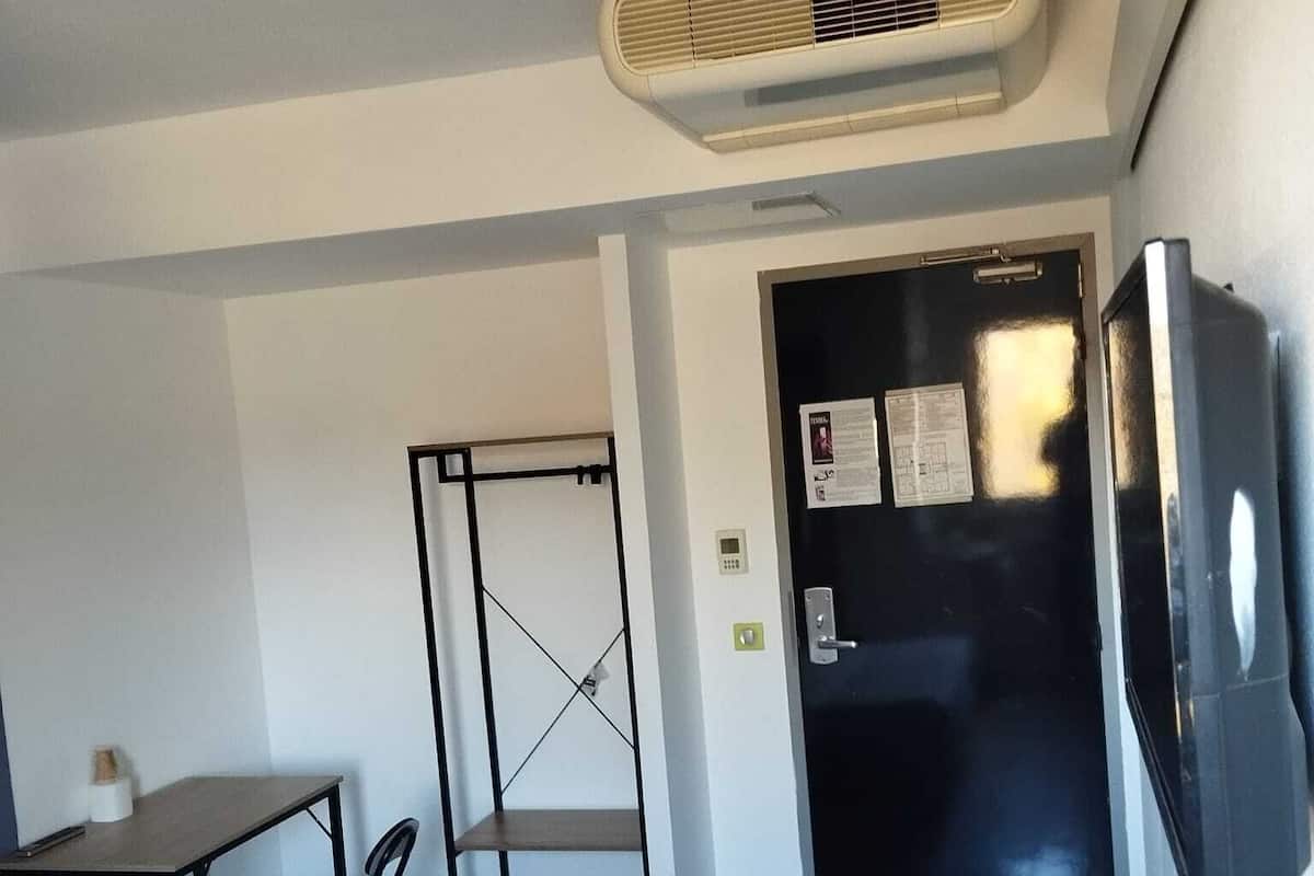 Une petite pièce, de taille modeste, comprenant un lit, un bureau, une chaise, une armoire noire et un téléviseur fixé au mur.