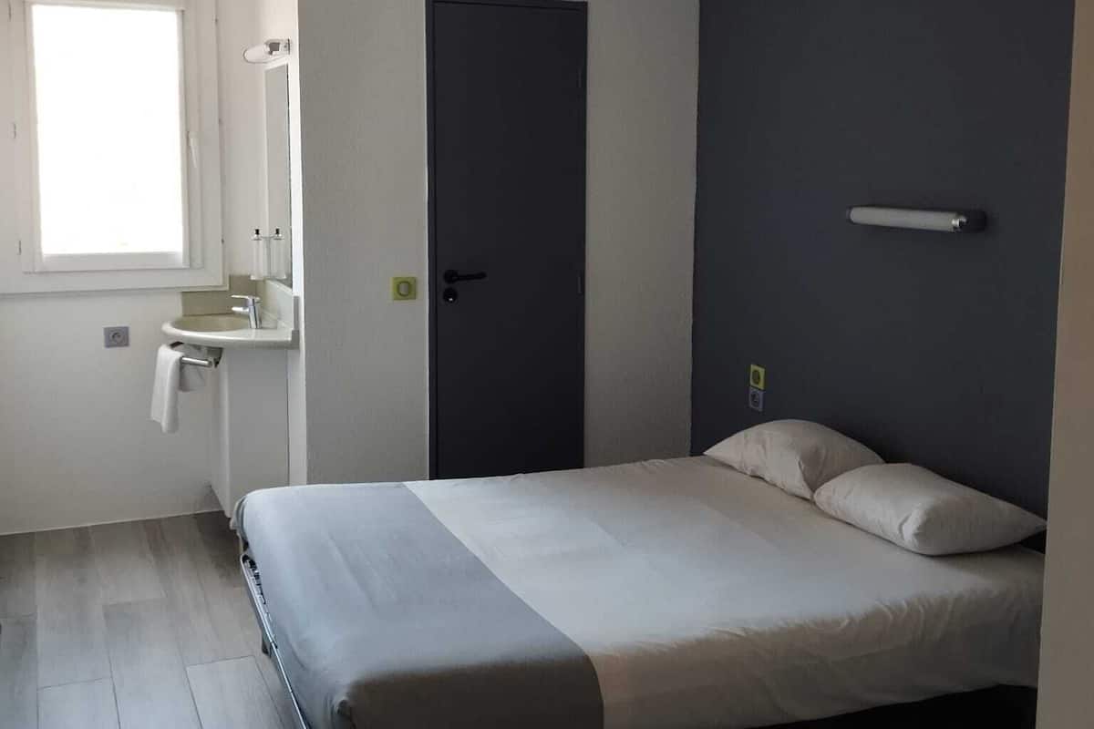 Une chambre à coucher comprenant un lit, une fenêtre, une porte et un petit coin salle de bain.