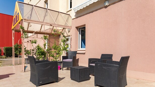 Un patio al aire libre con mobiliario de mimbre, una pérgola y un edificio con pared rosa.