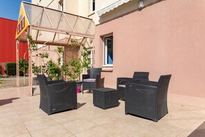 An outdoor patio with wicker furniture, a pergola, and a building with a pink wall.