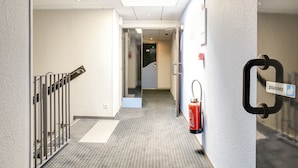 Pasillo de hotel con extintor, barandilla y puerta con letrero.