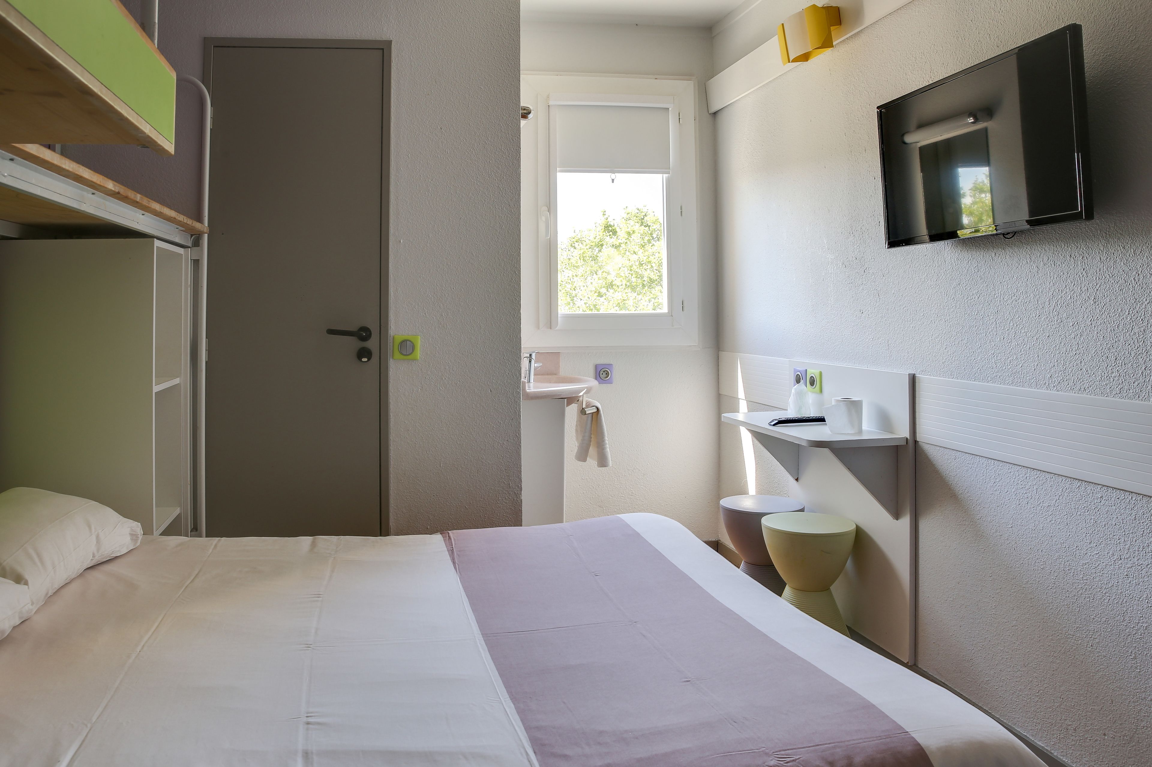 Ein Hotelzimmer mit Bett, Nachttisch, Spiegel, Fernseher und Fenster.
