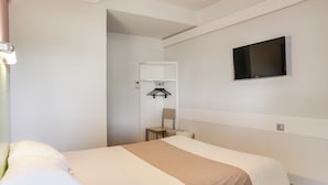 Habitación de hotel con cama, televisor montado en la pared, perchero y una mesita.