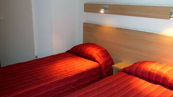Habitación de hotel con dos camas, cada una con ropa de cama roja, cabeceros de madera y un pequeño estante de madera encima de las camas.