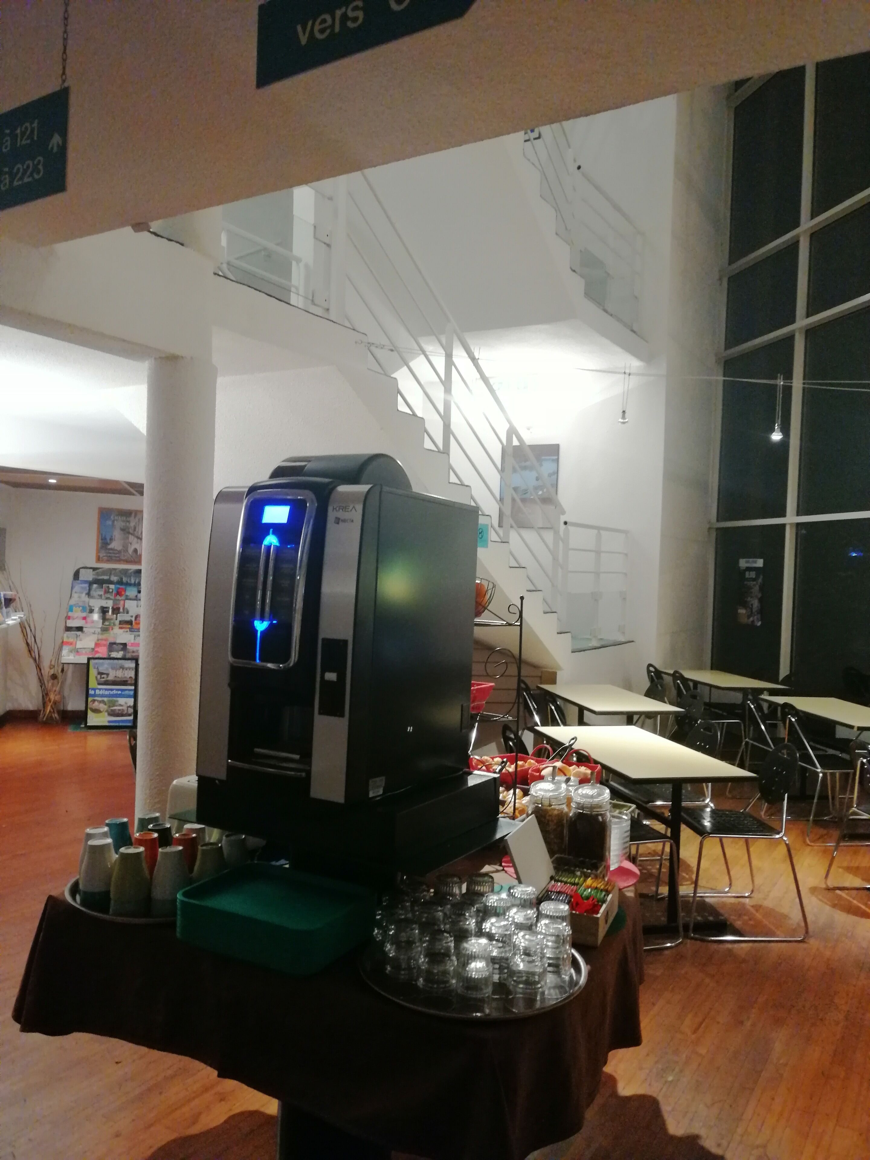 A coffee machine on a table with various cups and condiments.