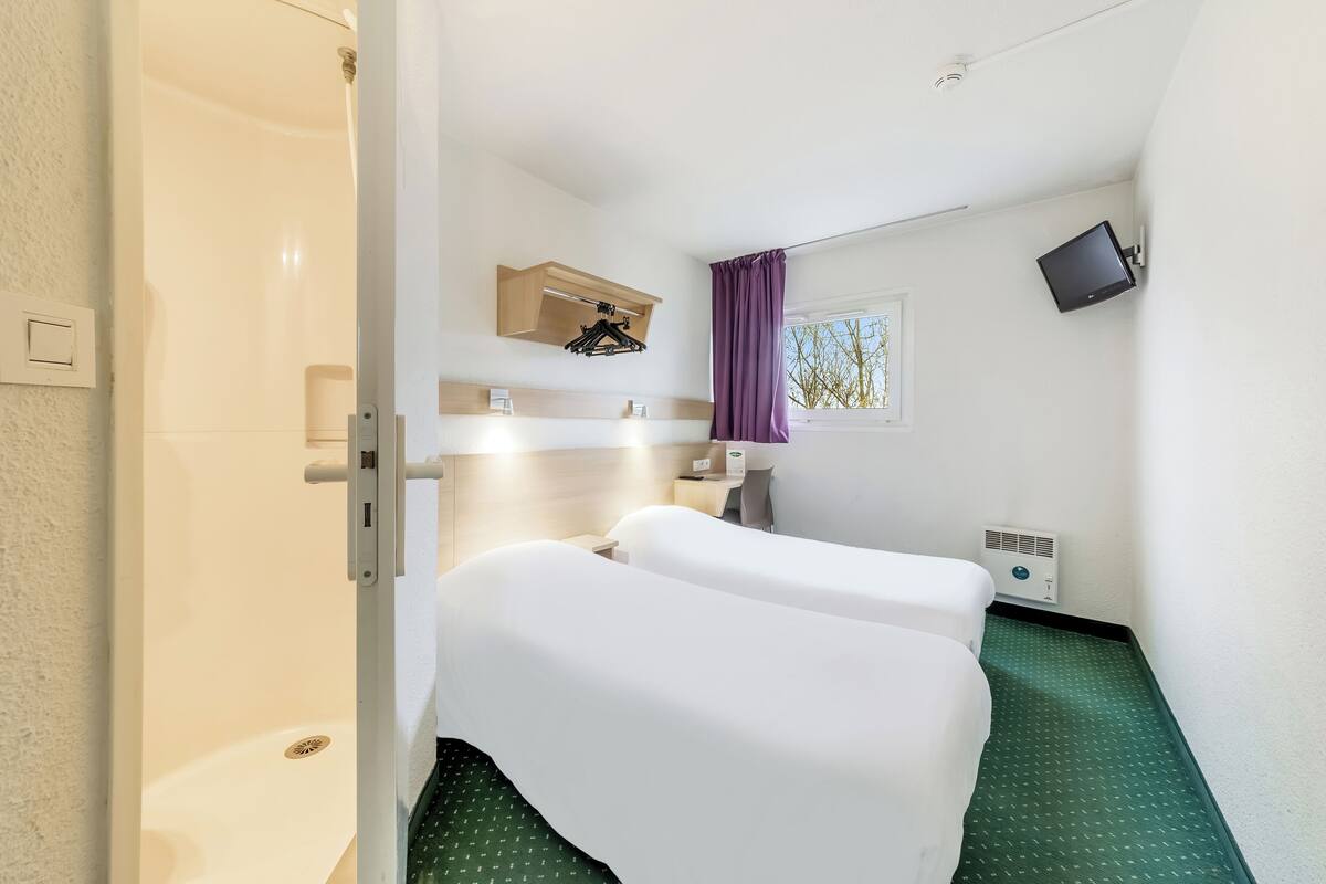 A hotel room with a shower, a bed, a TV mounted on the wall, and a window with curtains.