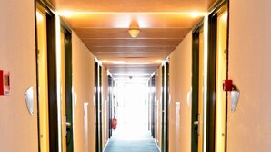 A hotel hallway with doors on both sides, a patterned carpet, and overhead lighting. - Mister Bed Chambray lès Tours (Chambray-les-Tours)