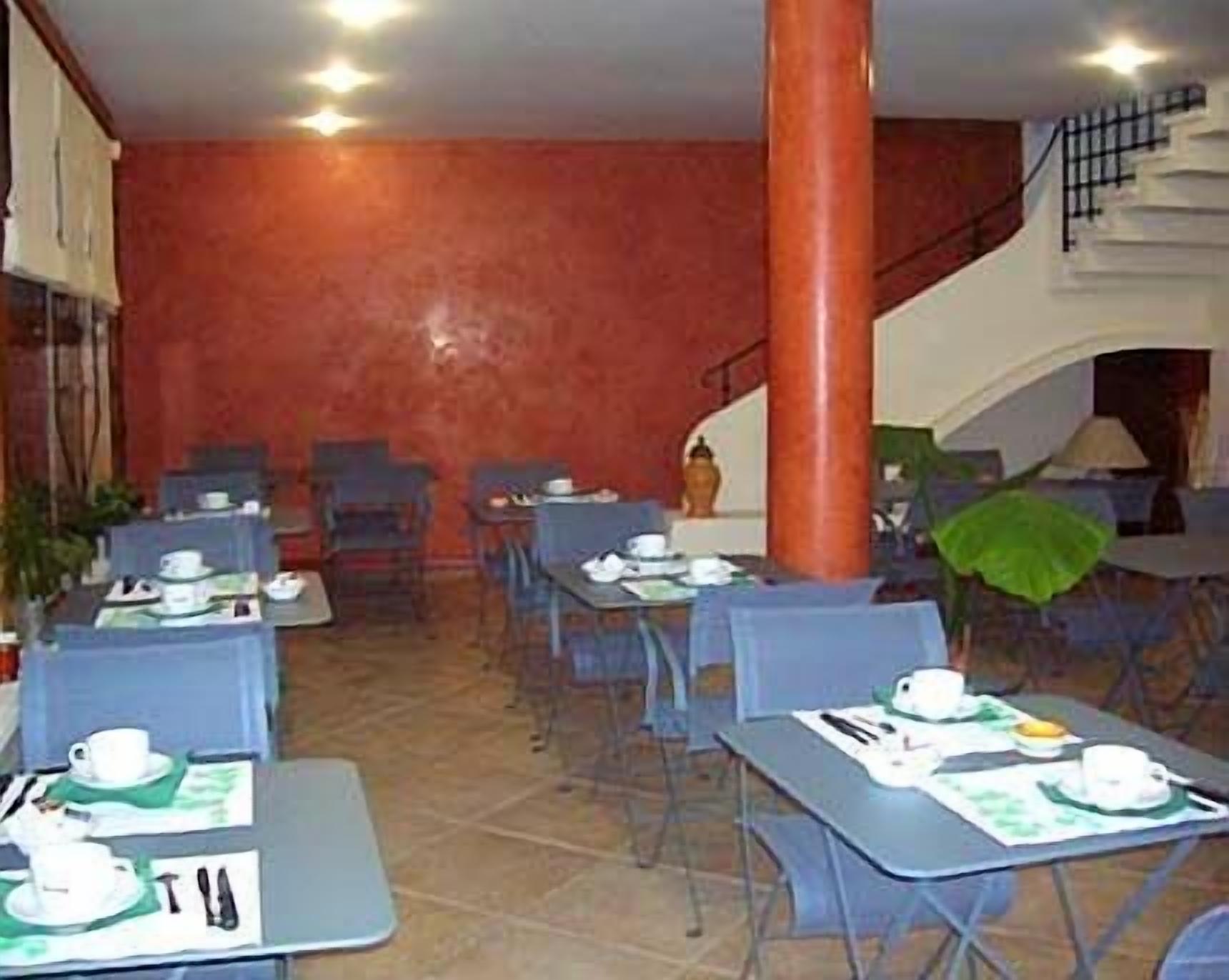 Un comedor con mesas dispuestas para comer, sillas y una escalera al fondo.