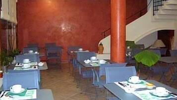 Un comedor con mesas dispuestas para comer, sillas y una escalera al fondo.