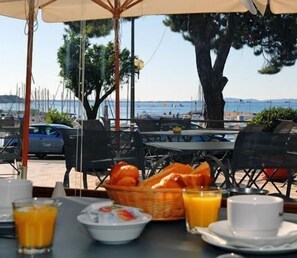 Un área de comedor al aire libre con mesas, sillas y vista al mar.