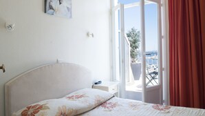 Quarto com cama, mesa de cabeceira, pintura e vista para uma varanda com mobiliário exterior.