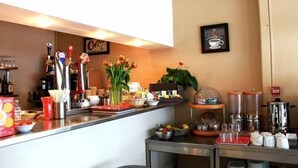 Espaço de café da manhã em hotel, com balcão, máquinas de café e diversas opções para o café da manhã.