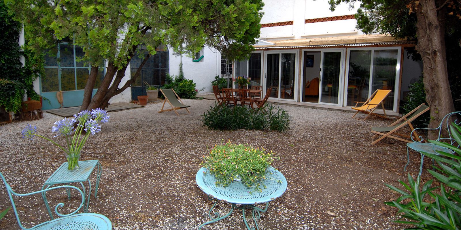 A patio area with a table and chairs, surrounded by gravel, and a building with a glass door in the background.