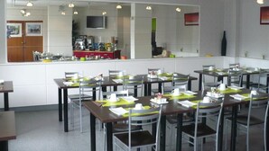 Comedor con mesas dispuestas para el servicio, cocina al fondo y un espejo grande que refleja el ambiente.